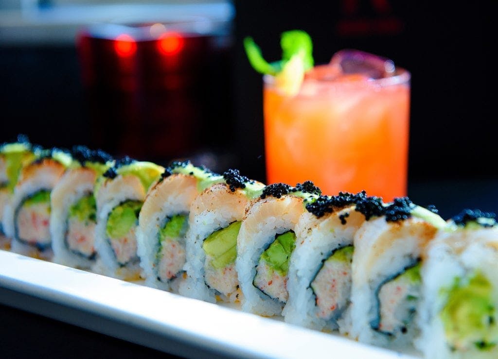 A picture of a colorful sushi roll and drink in the background hand crafted by sushi chefs at Japonessa.