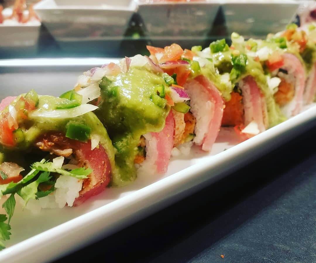 Picture of a Verde la Masa sushi roll. Spicy yellowtail, jalapeno, cilantro, gobo, topped with 7 spice tuna, tomatillo salsa, and pico.
